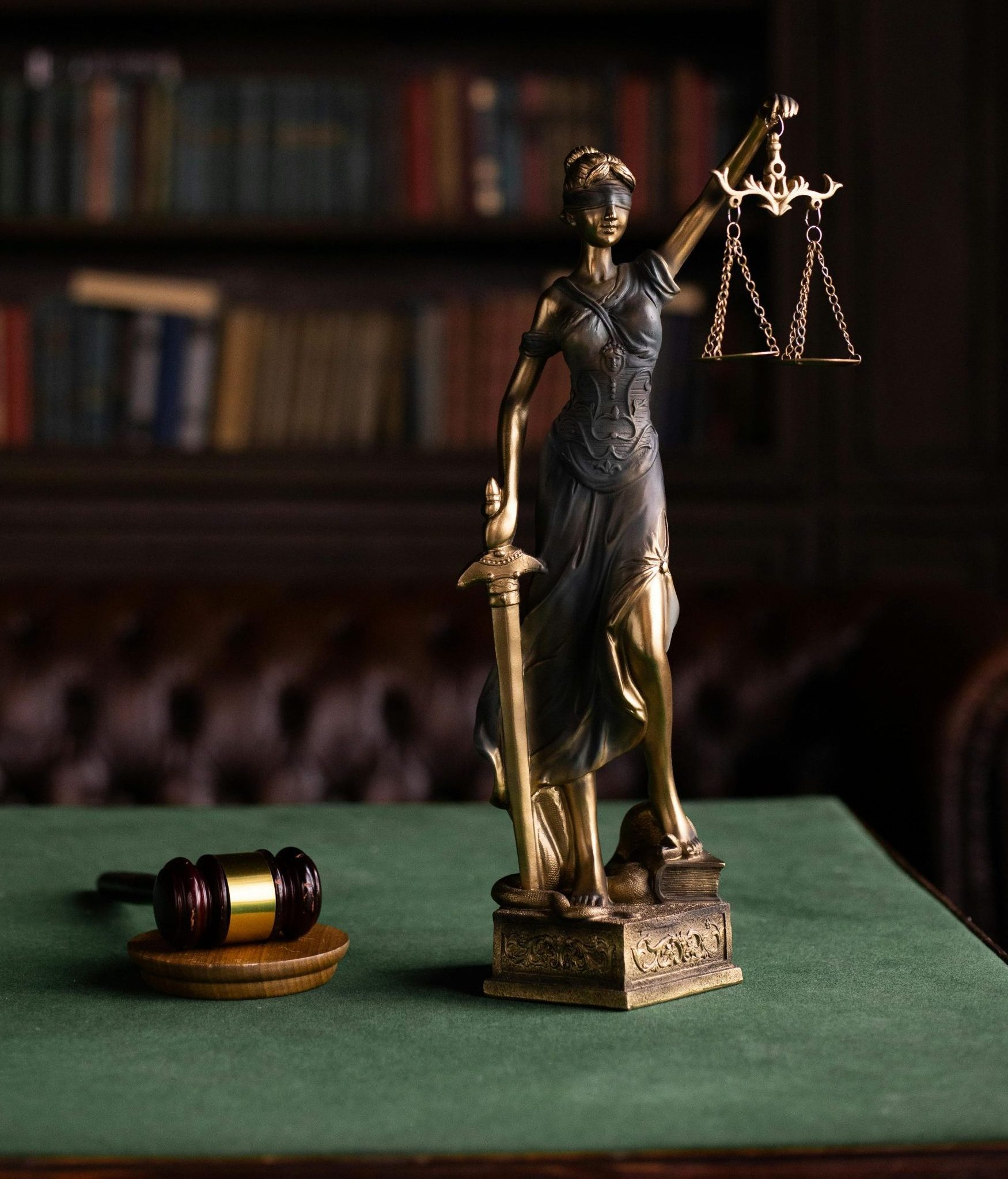 Justitia und Hammer auf einem Tisch in der klassischen Kulisse einer juristischen Bibliothek.